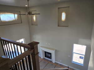 Two-story interior featuring a wood-finish staircase with black balusters, a ceiling fan with integrated lighting, a fireplace with a white mantel, and multiple windows