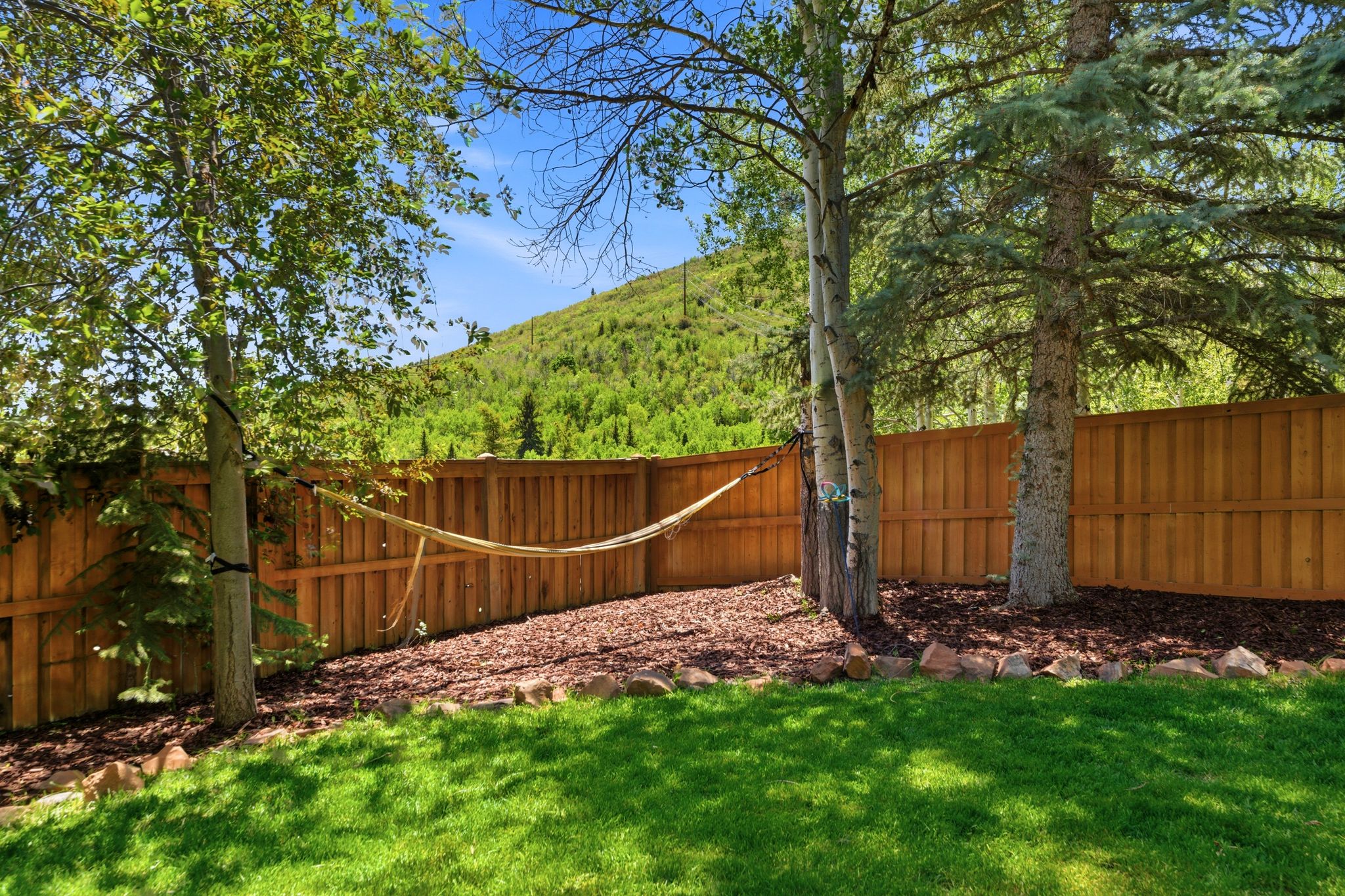 Expansive backyard featuring a manicured lawn, established trees, a wood privacy fence, and a mulched garden bed with rock edging