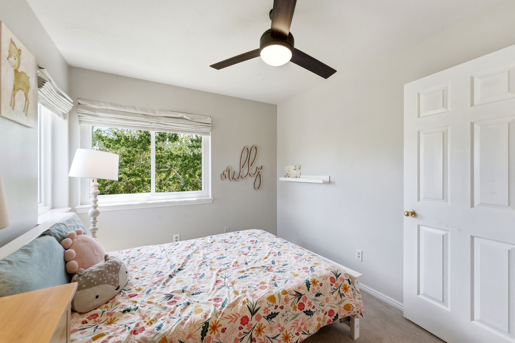 Upper Bedroom 1 with light gray walls, a window with a green outdoor scenery, a dark-toned ceiling fan with integrated lighting, and light-colored flooring