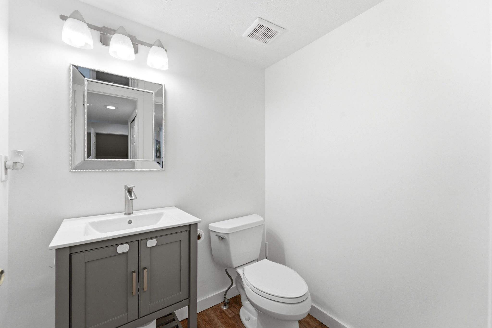 Bathroom featuring a gray vanity with an integrated white sink, a rectangular framed mirror, and a three-light vanity fixture