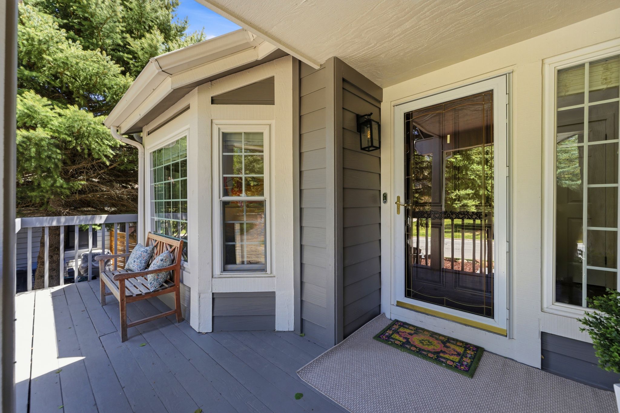 Covered front porch featuring a storm door, bay window, gray siding, and a deck with railings