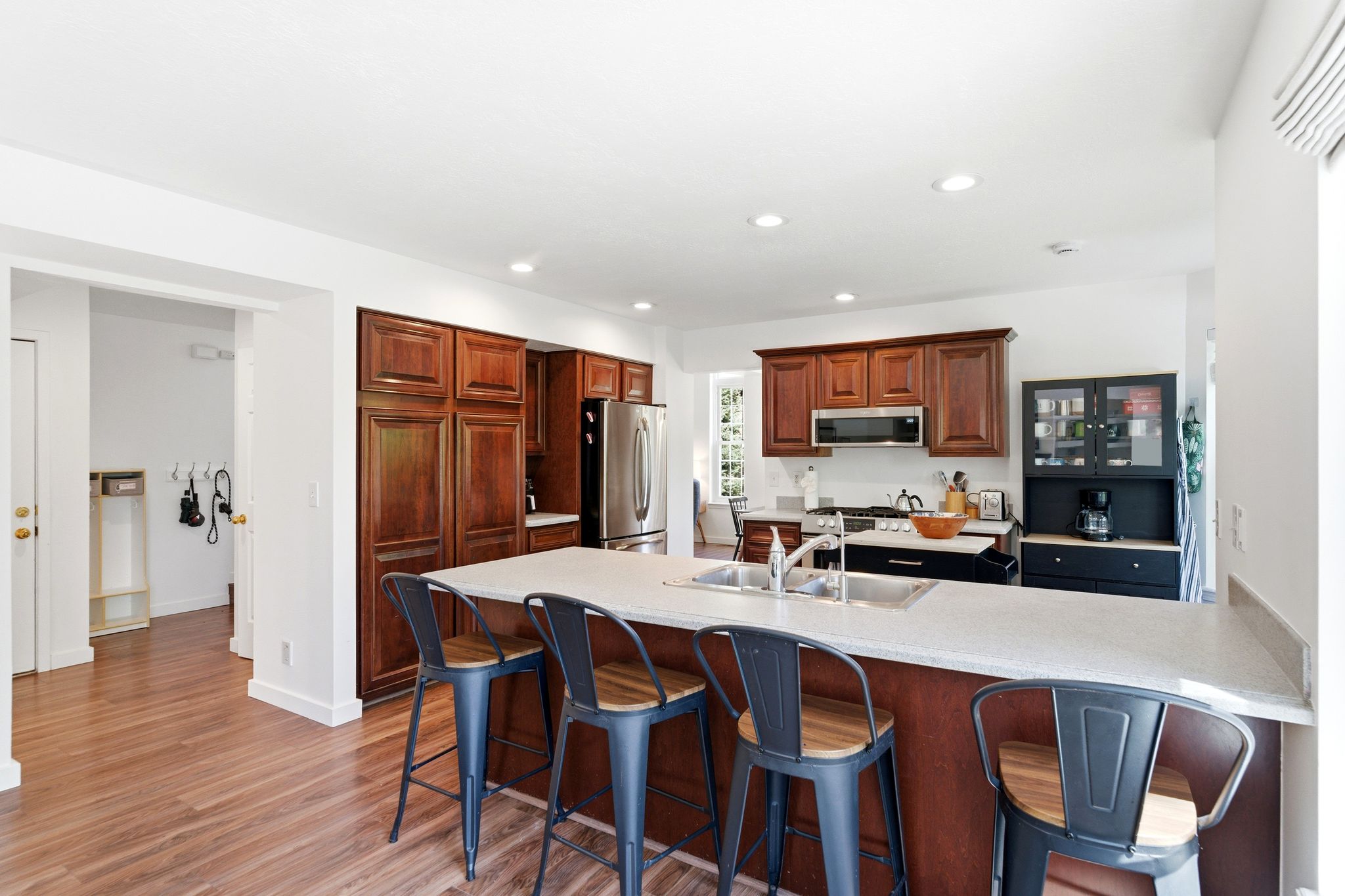 Contemporary kitchen featuring a large central island with seating, LVP flooring, recessed lighting, stainless steel appliances, and abundant wood cabinetry