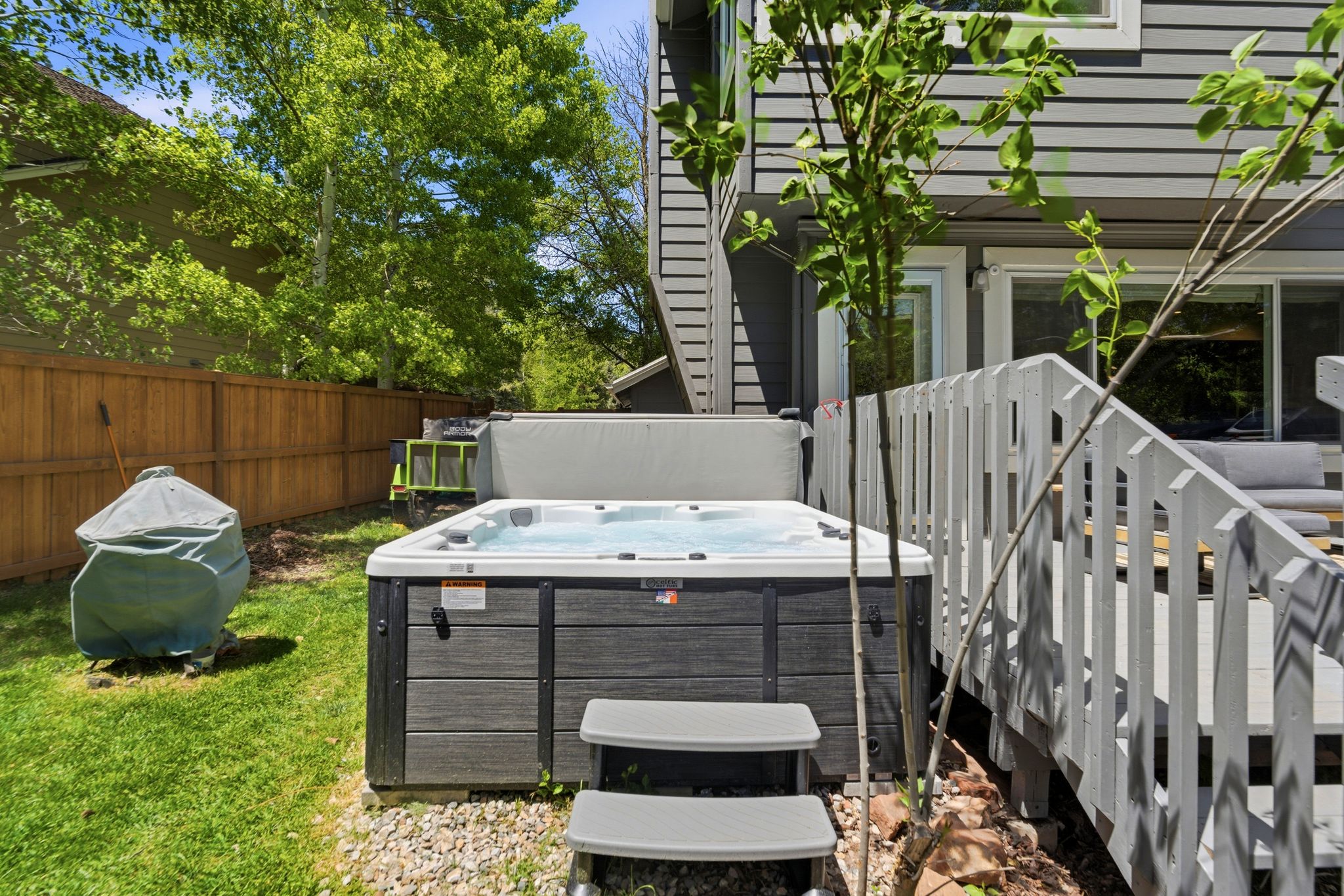 Outdoor hot tub with two steps, wood privacy fence, and a multi-level wood deck with white railings