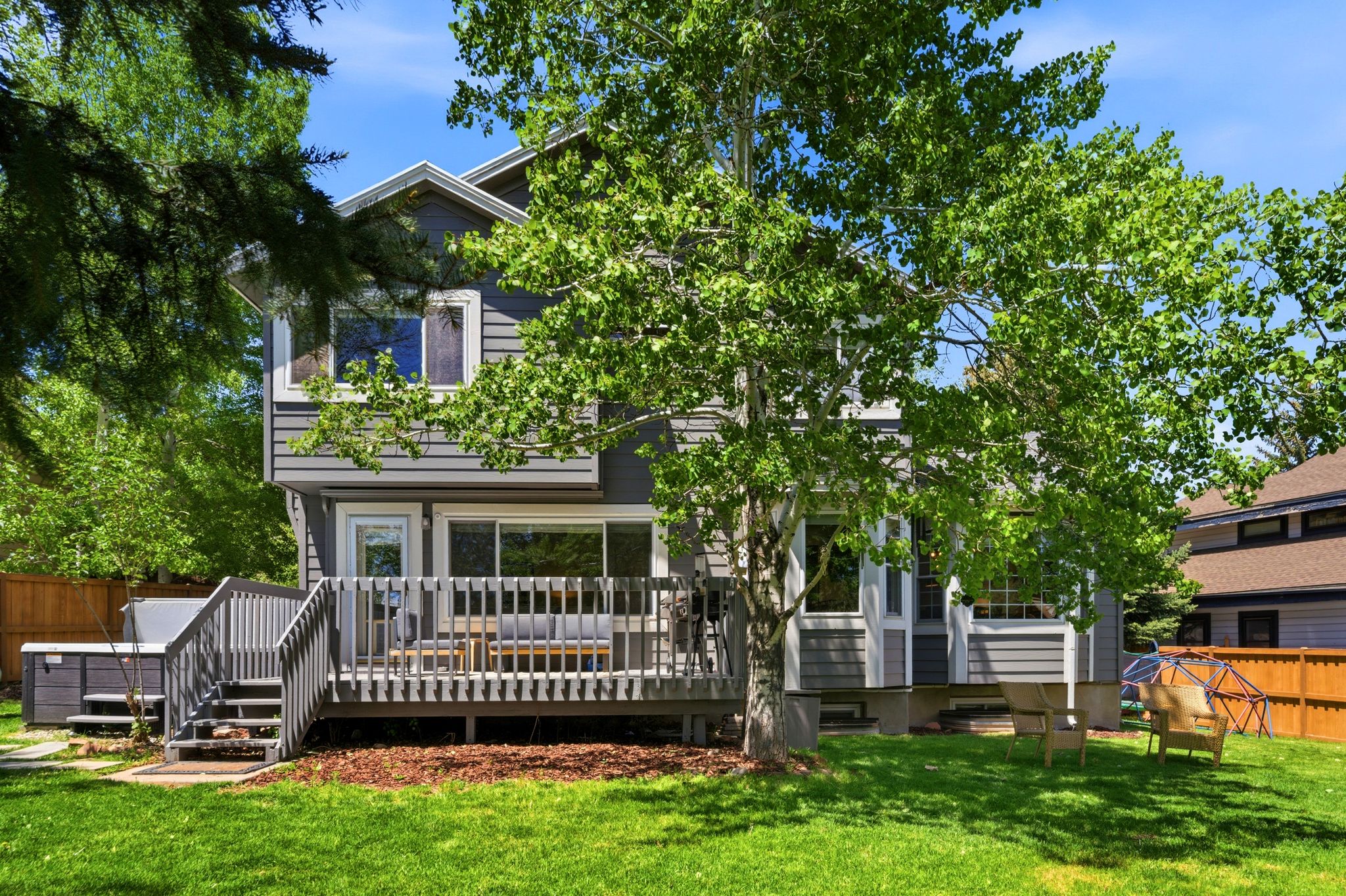Expansive backyard featuring a manicured lawn, a multi-level deck with built-in railing, and mature trees