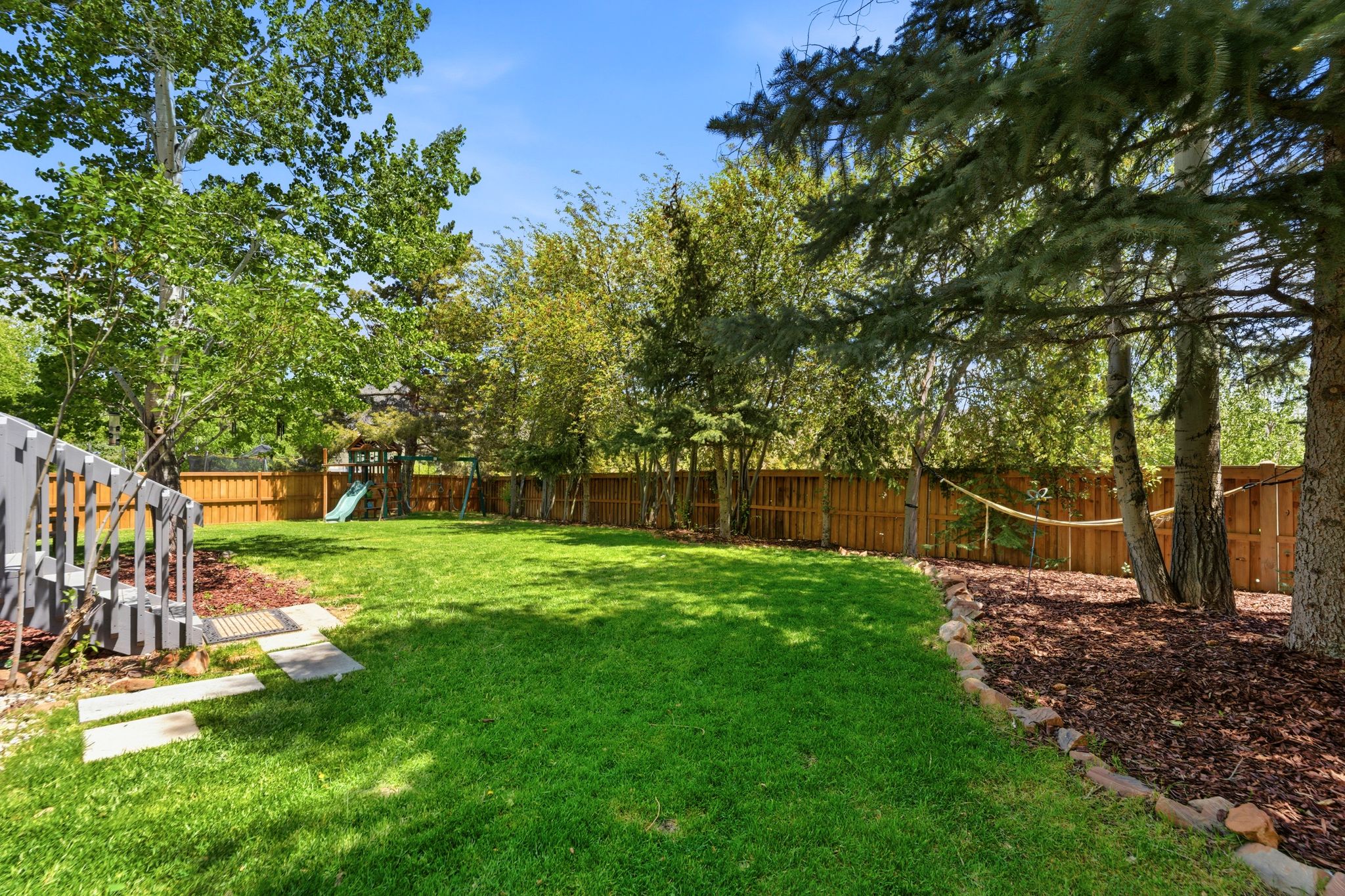Expansive backyard featuring a manicured lawn, full wood privacy fencing, mature trees, and a mulched garden bed