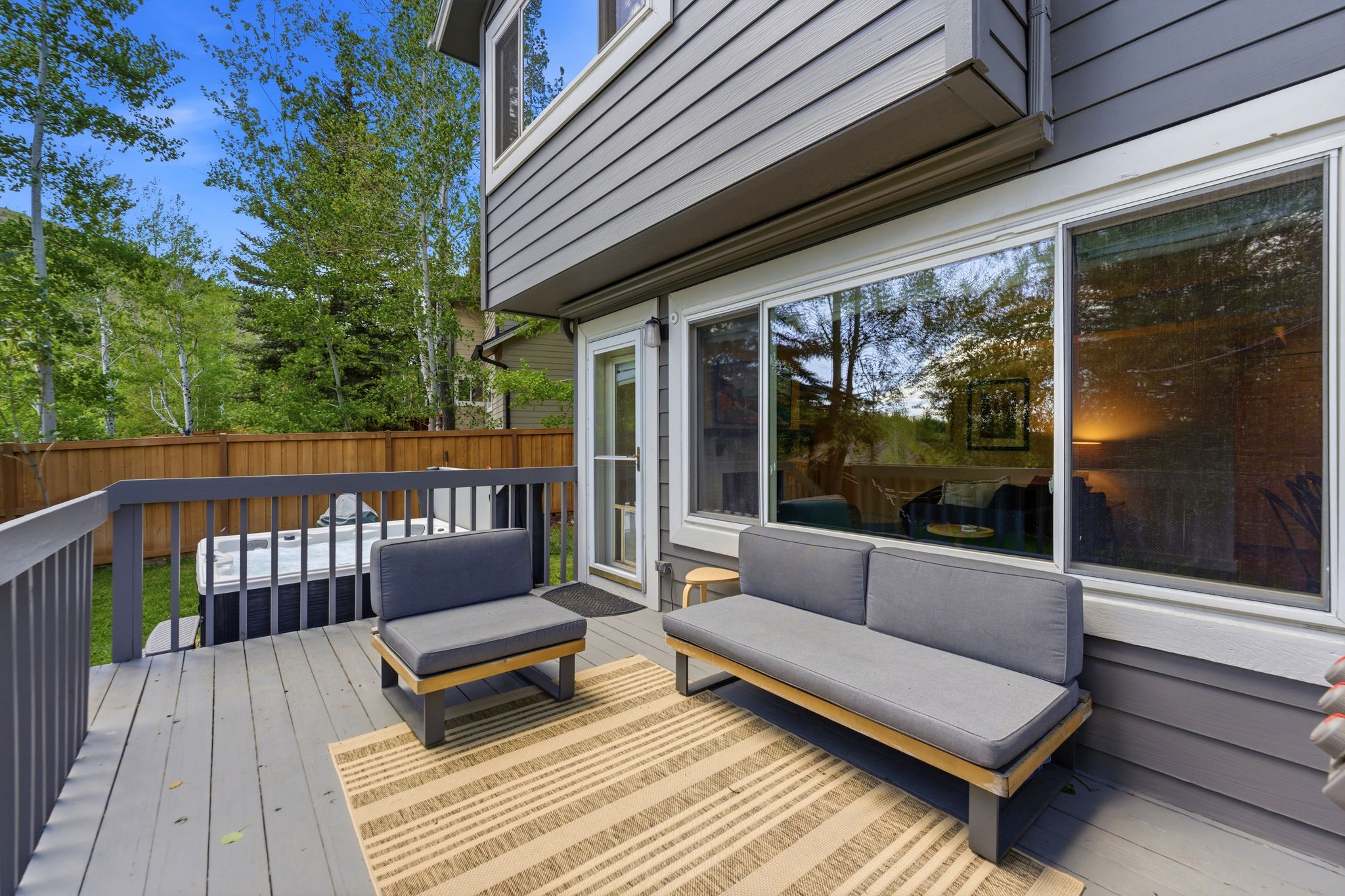 Expansive outdoor deck featuring a hot tub, wood fencing, and direct access to interior spaces through a glass door and large sliding windows