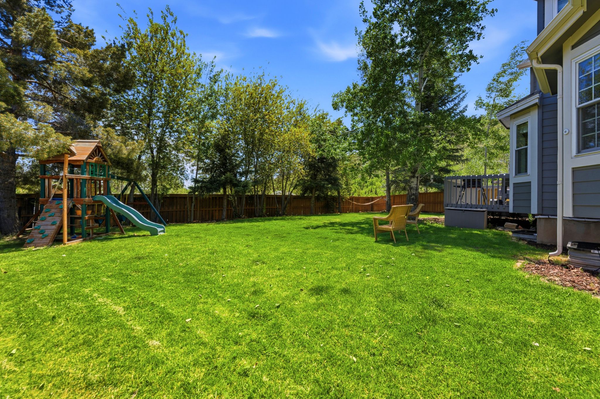 Fully Fenced yard with Expansive green lawn with mature trees and a wood privacy fence