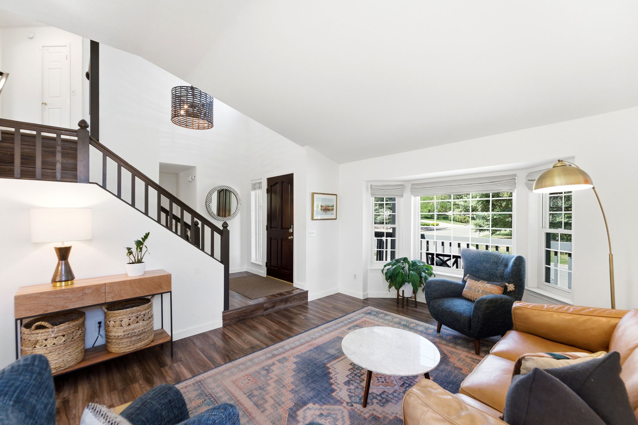 Living room featuring LVP flooring, a prominent bay window, and a dark wood staircase with spindle railing