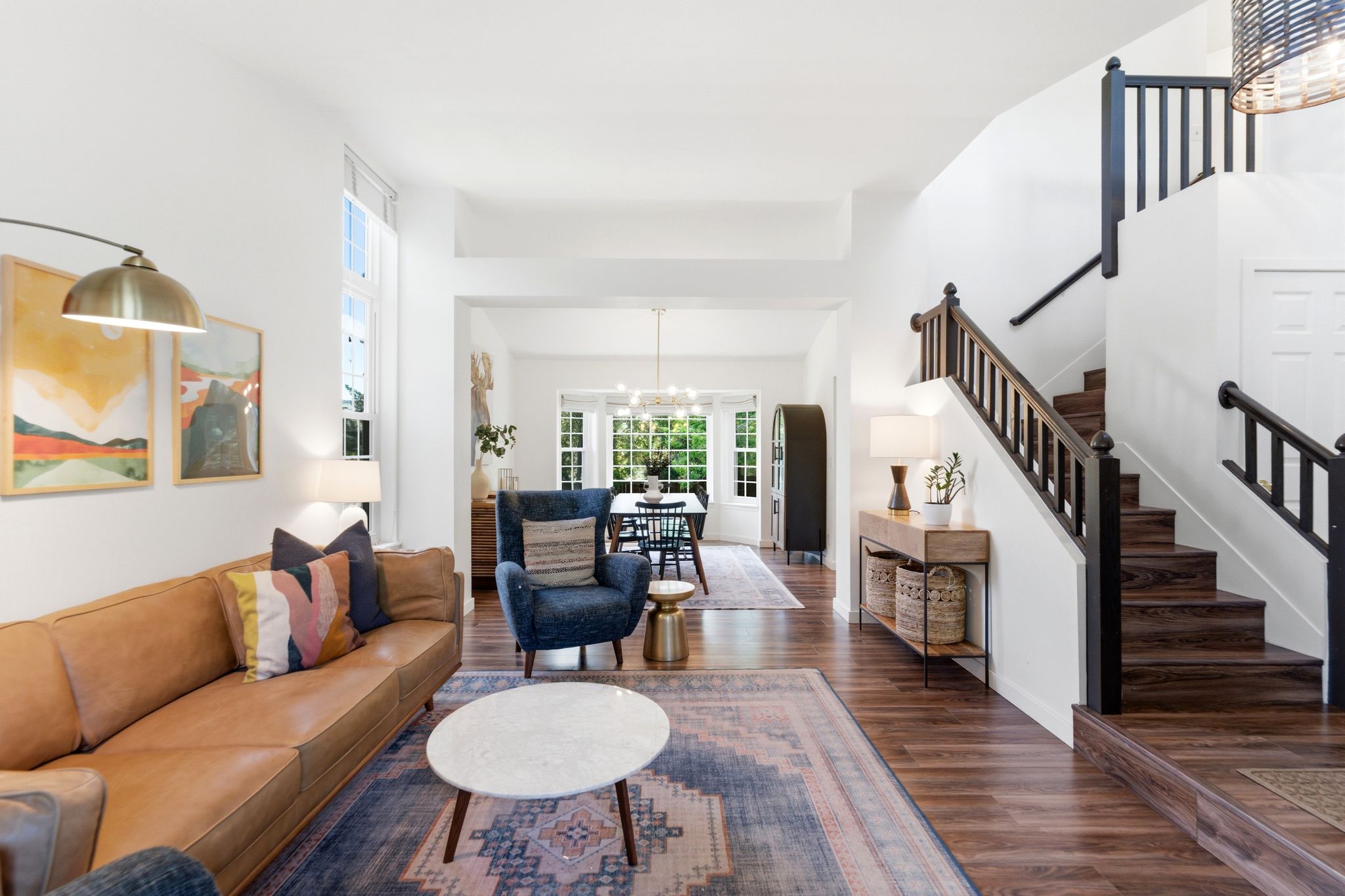Open-concept living space featuring LVP flooring, a contemporary staircase with dark wood newel posts and railings, and high ceilings