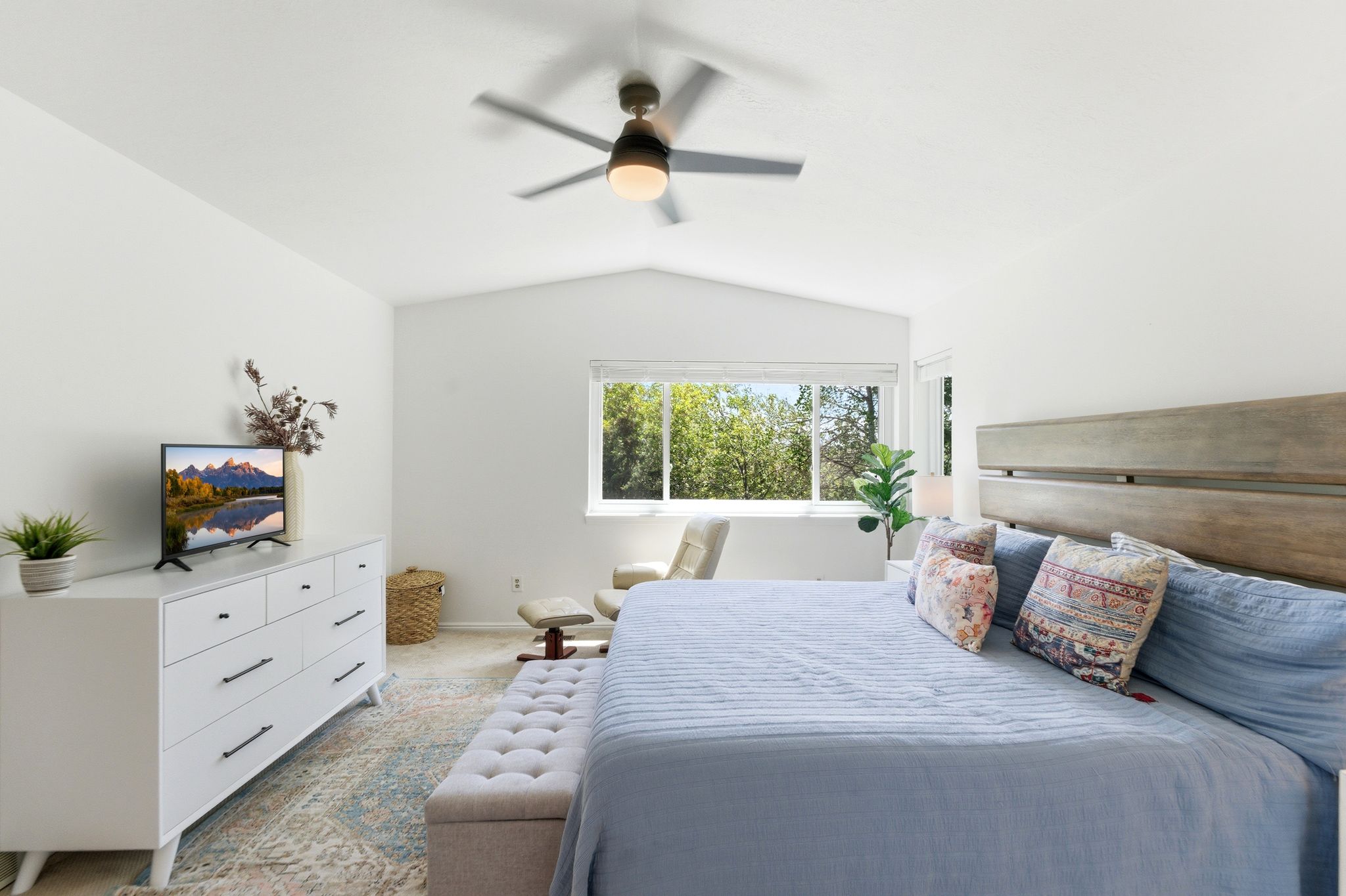 Primary bedroom featuring vaulted ceilings, a contemporary ceiling fan with integrated lighting, a large window with natural light, and a substantial wood-finish headboard