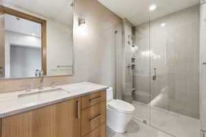 Modern bathroom featuring a clear glass shower enclosure, a wood-finish vanity with an undermount sink, a stone countertop, honeycomb tile backsplash, and polished chrome fixtures
