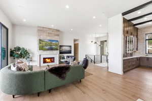 Expansive living area featuring light wood-finish flooring, a stone-clad fireplace, recessed lighting, and a built-in wet bar with dark wood cabinetry