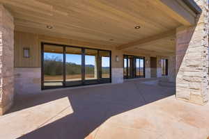 Expansive covered patio featuring a wood-finish ceiling with recessed lighting, stone-clad columns, and multiple sets of large glass sliding doors