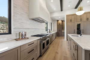 Gourmet kitchen featuring a large central island, light wood-finish cabinetry with dark hardware, stainless steel appliances, a stacked stone backsplash, and recessed lighting