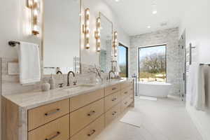Bathroom featuring a freestanding soaking tub, large picture window, a double vanity with stone countertops, wood-finish cabinetry, and a walk-in shower with glass enclosure