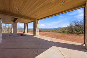 Expansive covered patio featuring a wood-panel ceiling, recessed lighting, and stone-clad support pillars