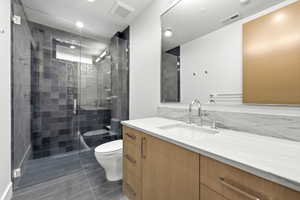 Bathroom featuring a frameless glass shower enclosure with dark tile, a floating light wood-finish vanity with an integrated sink, a white countertop, and a large wall-mounted mirror