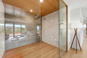 Room featuring glass partition, wood-finish flooring, wood plank ceiling, recessed lighting, and a textured stone accent wall