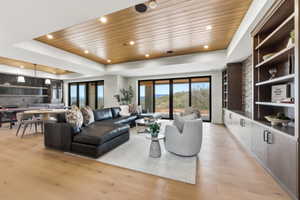 Spacious living area featuring wood-finish flooring, a wood-paneled ceiling with recessed lighting, integrated shelving with cabinetry, and large black-framed sliding glass doors