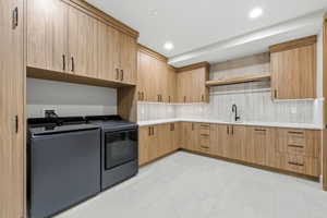 Spacious utility room featuring extensive wood-finish cabinetry, light-toned countertops, a black sink with a matte black faucet, and light-colored tile flooring