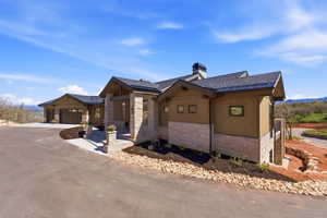 Contemporary exterior featuring stone veneer and horizontal siding, a dark asphalt shingle roof, a two-car garage with wood-finish doors, and a stone-clad entry with columns and steps