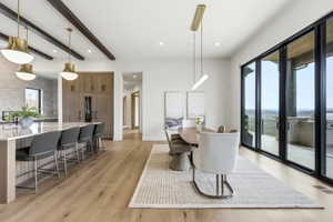 Expansive open-concept living area featuring light wood-finish flooring, a contemporary dining space with a linear pendant light, and a kitchen island with seating