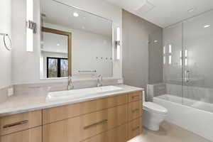 Contemporary bathroom featuring a light wood-finish double vanity with a rectangular basin, stone-finish countertop, and wall-mounted sconce lighting