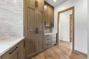 Custom cabinetry with matte black hardware, light wood-finish flooring, and a white countertop with a stone backsplash