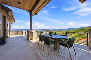 Expansive outdoor patio featuring large format tile flooring, a built-in outdoor grill, a wood-paneled ceiling, and stone-clad columns
