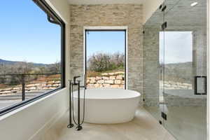 Spa-inspired bathroom featuring a freestanding soaking tub with floor-mounted fixtures, a frameless glass shower enclosure, and stacked stone accent walls