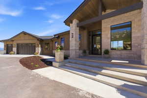 Stone veneer and wood-finish siding exterior with multi-panel garage doors, a covered entry, large picture window, and concrete entry steps