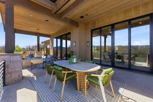 Spacious outdoor patio featuring a wood plank ceiling with recessed lighting, stone-clad pillars, and a metal railing