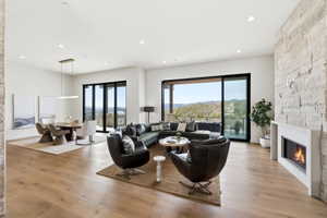 Open-concept living area with wood-finish flooring, a contemporary fireplace featuring a stone accent wall, and expansive glass doors opening to a scenic mountain landscape