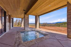 Outdoor patio featuring an integrated hot tub, natural stone-clad pillars, wood-paneled ceiling, and sliding glass doors