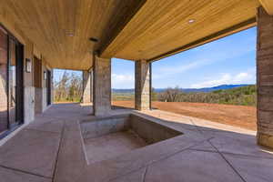 Expansive covered patio featuring a wood-finish ceiling with recessed lighting, stone-clad support columns, concrete flooring, and an integrated sunken area