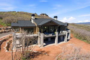 Multi-level residence featuring a dark shingle roof, multiple chimneys, and extensive outdoor deck space supported by stone columns