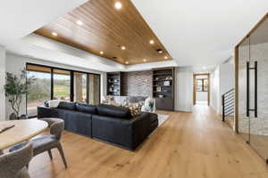 Spacious living area featuring light wood-finish flooring, a recessed wood-paneled ceiling with integrated lighting, and a stone accent wall