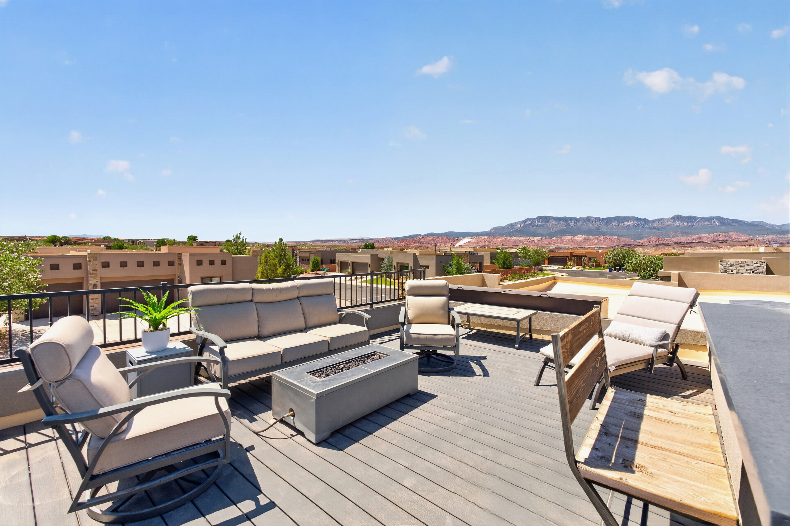 Expansive rooftop deck featuring composite decking, a built-in privacy wall, black metal railings, a stone-finish fire pit, built in bar and distant mountain scenery. Perfect for evening gatherings and star gazing.