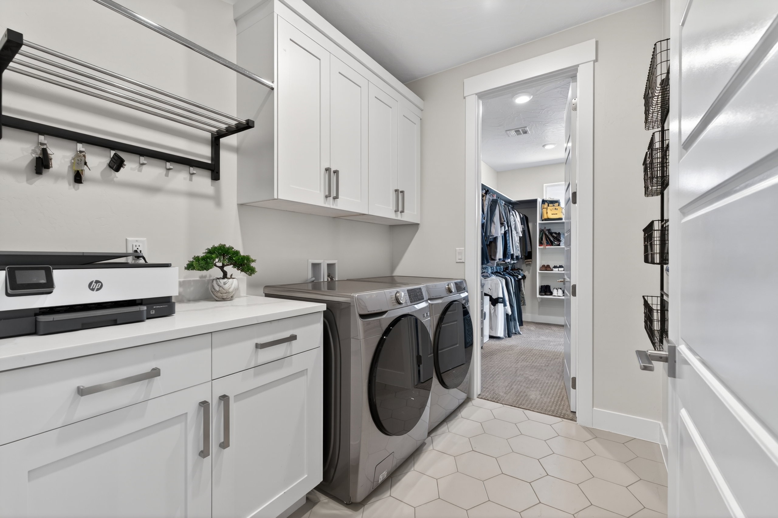 Dedicated laundry area attached to master suite, featuring hexagon tile flooring, white shaker cabinetry with brushed nickel hardware, and light-tone countertops