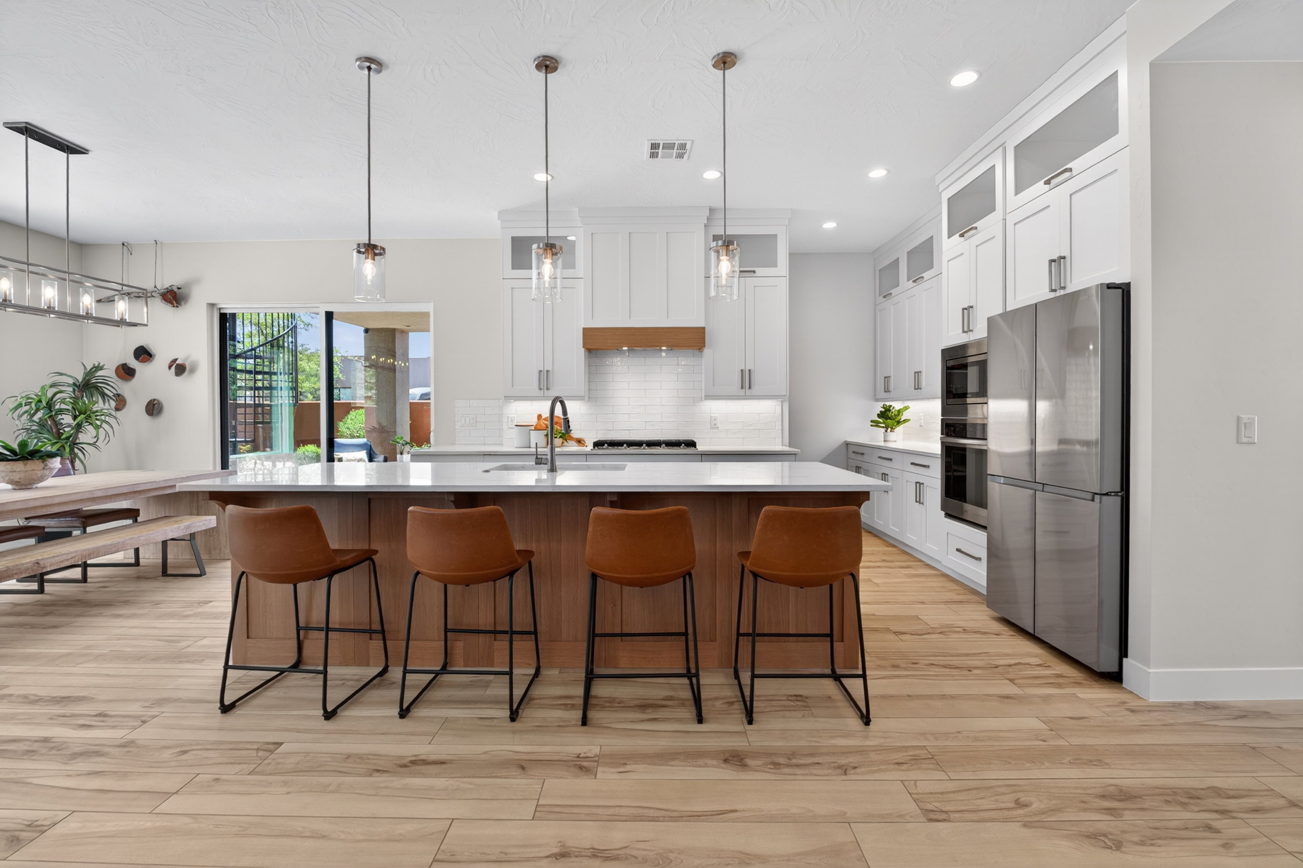 Expansive kitchen featuring a large central island with seating, white shaker cabinetry, stainless steel appliances, and wood-finish flooring