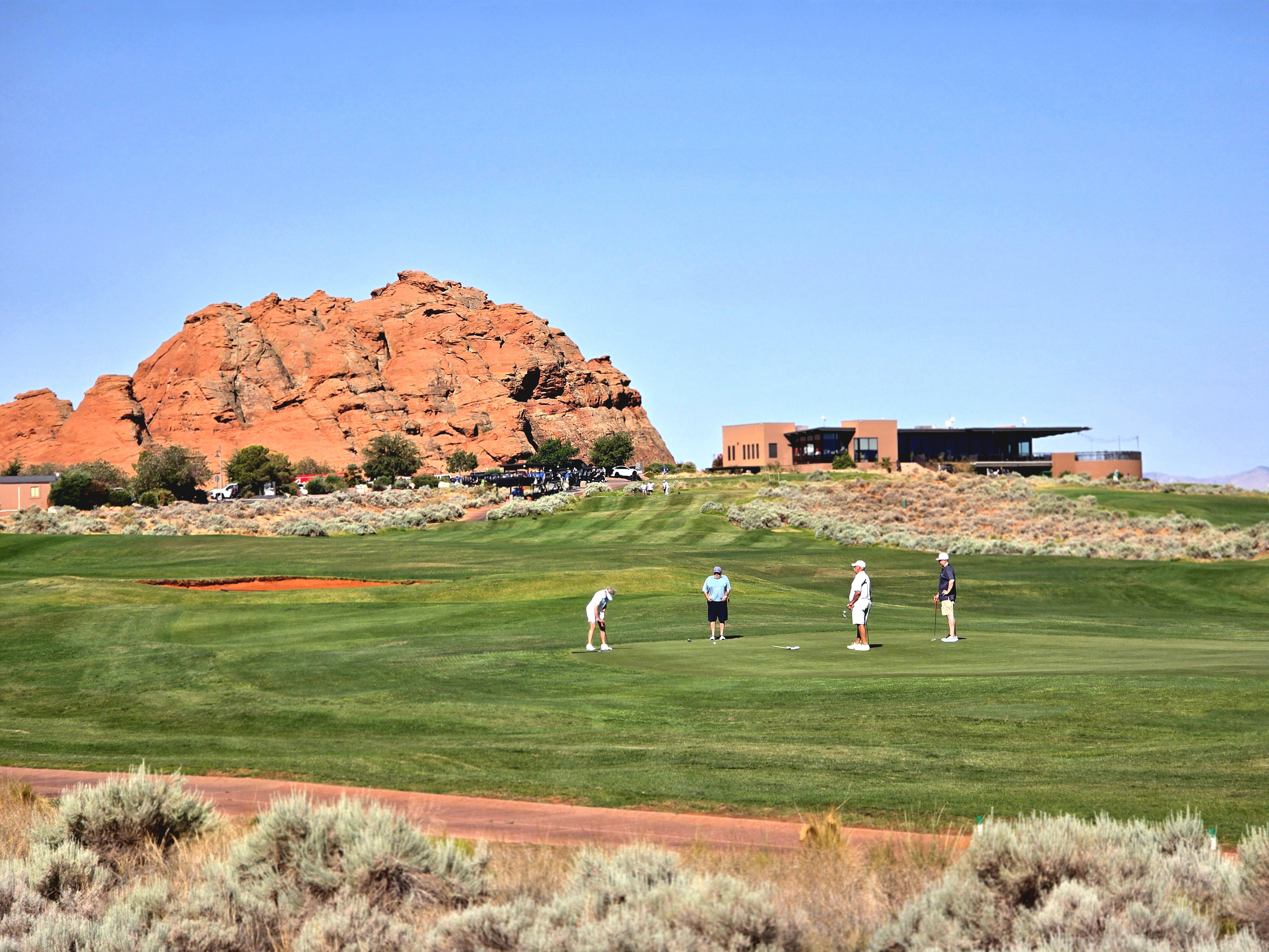Expansive Sand Hollow Resort golf course with a modern clubhouse and a prominent red rock formation backdrop