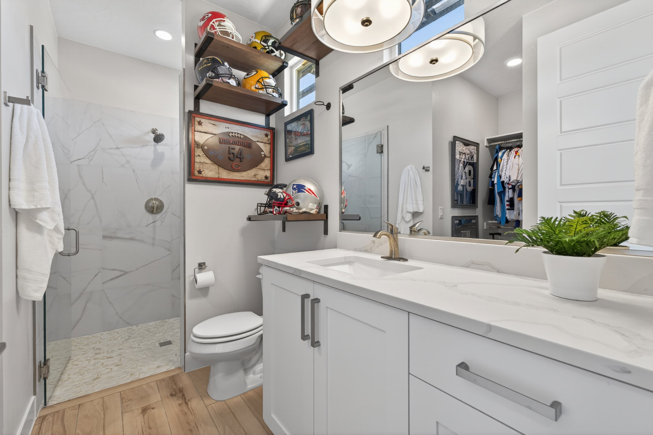 Bathroom featuring a glass-enclosed shower with large format marble-look tile, a single vanity with a white countertop, light wood-finish flooring, and built-in shelving