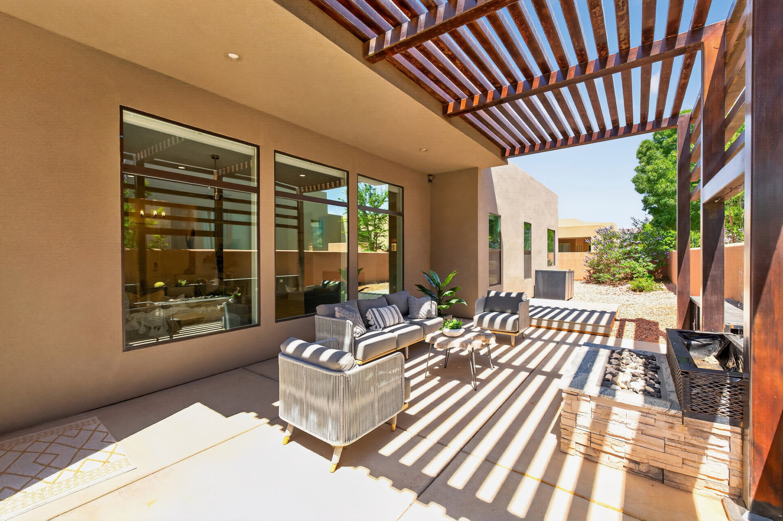 Expansive patio featuring a wooden pergola, stone-clad fire pit, large format tile flooring, and outdoor lighting for evening get togethers.
