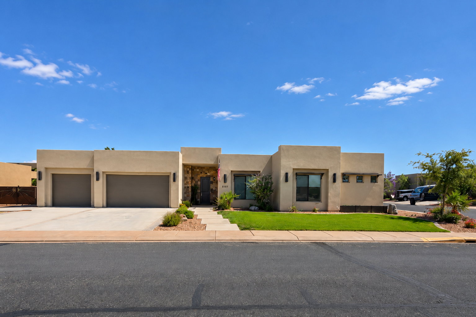 Contemporary stucco exterior featuring a stone accent entry, two-car garage, concrete driveway, and front landscaping with grass and desert plants