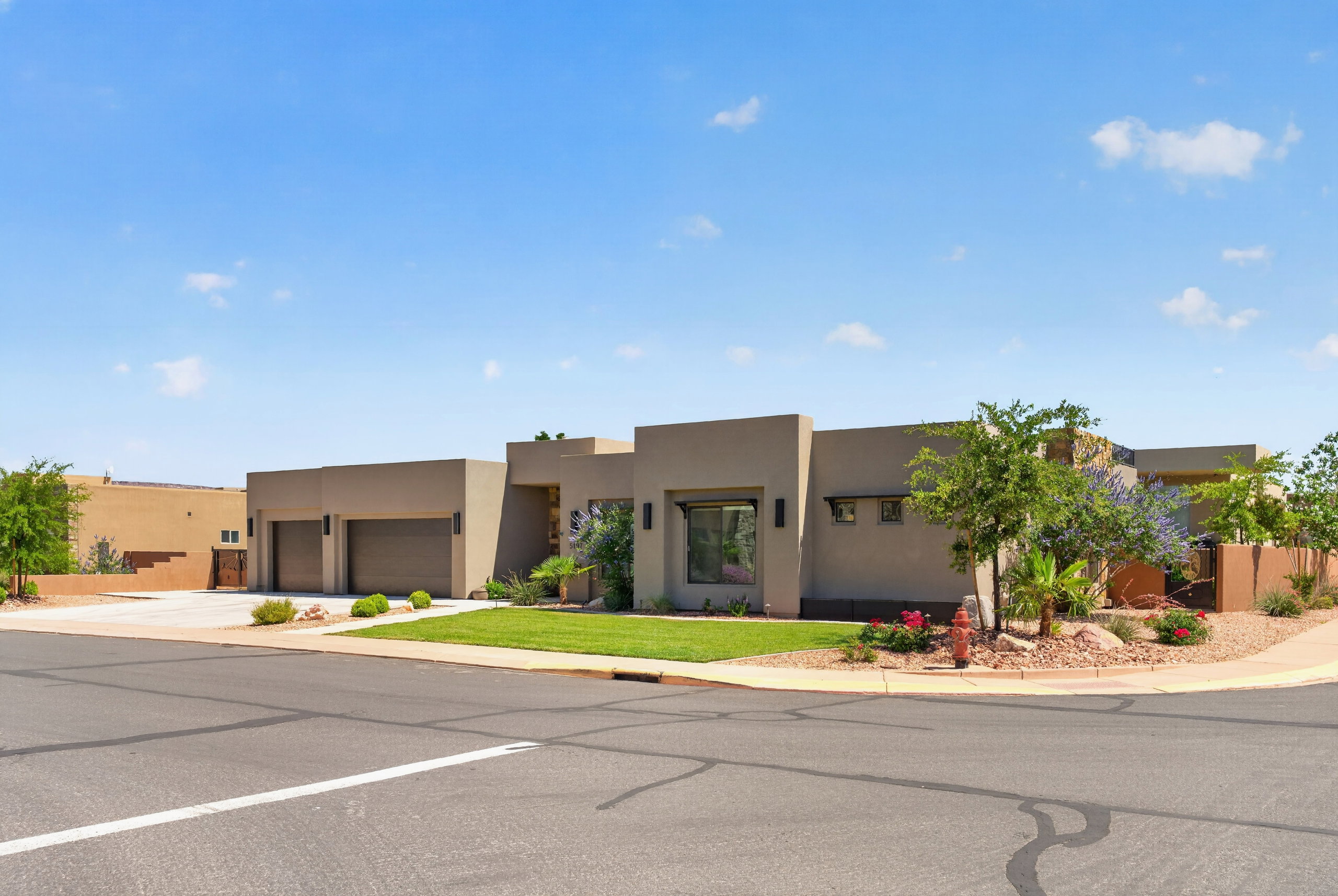 Contemporary stucco exterior featuring a two-car garage, mature landscaping, and a manicured lawn