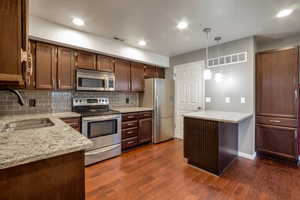 Kitchen featuring wood-finish flooring, granite countertops, stainless steel appliances, a tiled backsplash, and recessed lighting