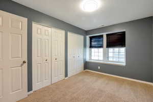 Bedroom featuring two panel doors, two bi-fold closet doors, two windows with dark blinds, and neutral carpet flooring