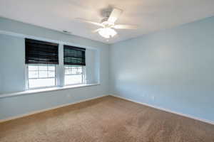 Carpeted room featuring light blue walls, two windows with dark blinds, a built-in window bench, and a ceiling fan with integrated lighting