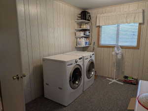 Laundry area featuring light-toned vertical paneling, a window with horizontal blinds and wood trim, and wall-mounted shelving for storage