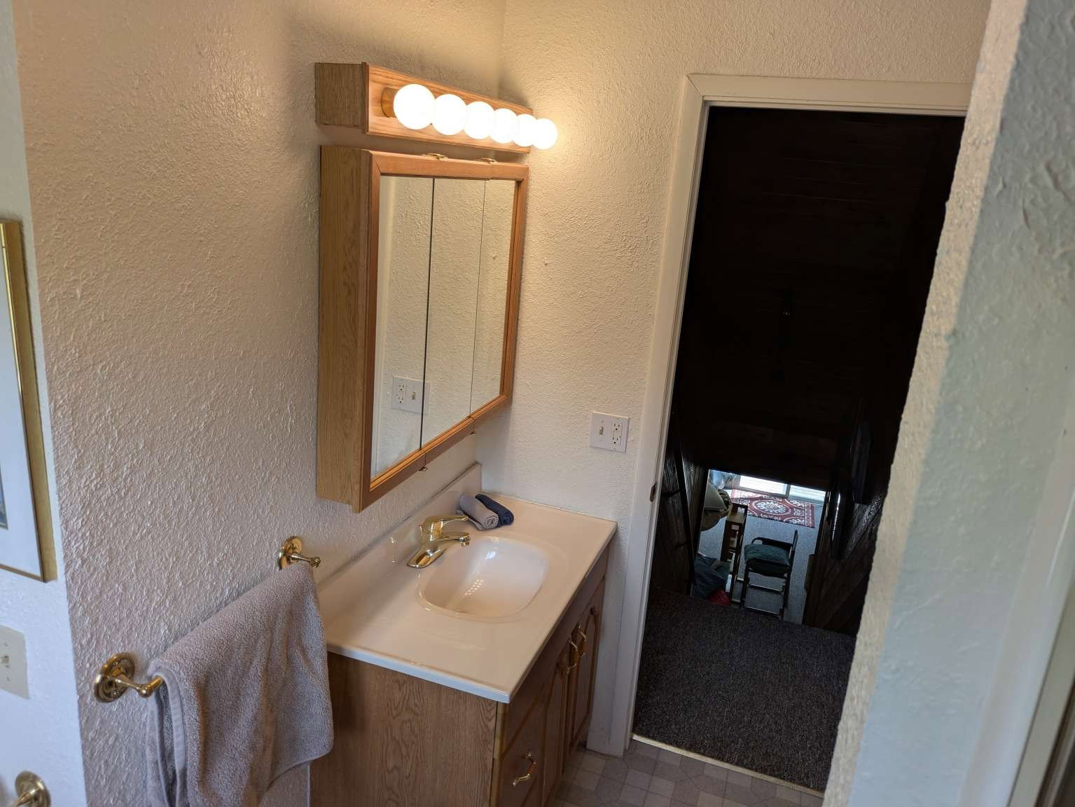 Bathroom vanity featuring a single basin sink, brass-finish faucet, and coordinating wall-mounted light fixture